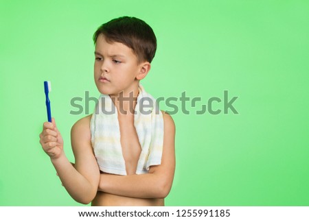 Boy brushing his teeth. Concept: children's health. Hygiene of children. Behind green background. He holds a toothbrush in his hand and thinks.