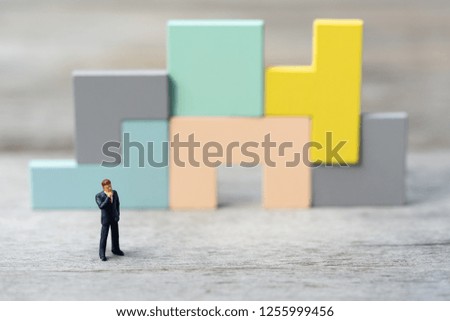 Miniature people: businessman thinking in front of wooden jigsaw puzzle icon, success, dealing, greeting and partner concept.