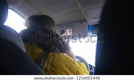 Young woman sitting in the car and looking on the mirror