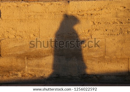 Close up urban view of the shadow of a lonely person walking in a french street. Dark grey human silhouette projected on a brown stone wall. Abstract picture of a pedestrian form on a rough surface.  