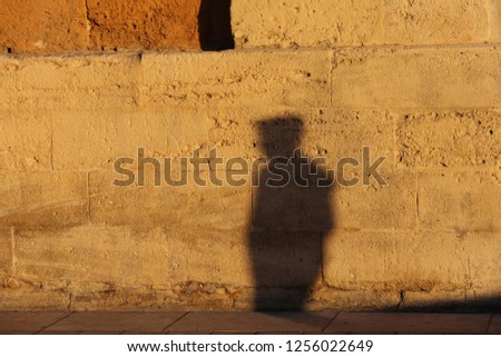 Close up urban view of the shadow of a lonely person walking in a french street. Dark grey human silhouette projected on a brown stone wall. Abstract picture of a pedestrian form on a rough surface.  