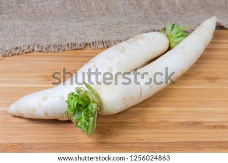 Two fresh washed daikon radishes with torn off haulm on a wooden bamboo cutting board at selective focus
