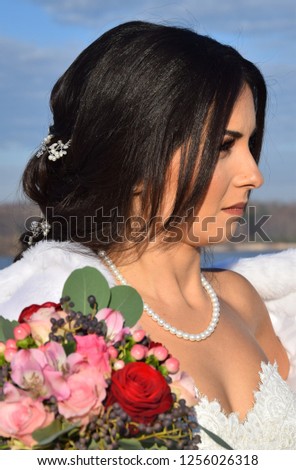 Gorgeous bride in a white wedding dress, veil, and bouquet on a beach in blue skies in summer