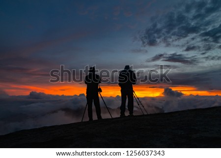 Two unidentified photographers take a photo of cloudy mountain landscape during sunrise.
