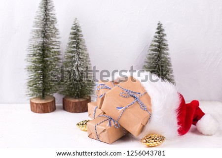 Wrapped boxes with presents, decorative golden pine cones in Santa hat  and fir trees on white textured background. Selective focus. Place for text. Winter holiday, Christmas, New Year.