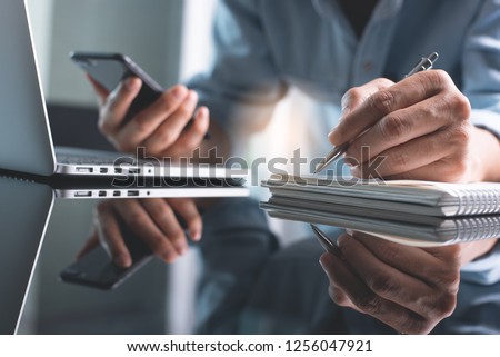 Business planning, Elearning concept. Casual business man writing on notebook and working on laptop computer in office. Man using mobile phone, studying online course via laptop and lecture on notepad Royalty-Free Stock Photo #1256047921