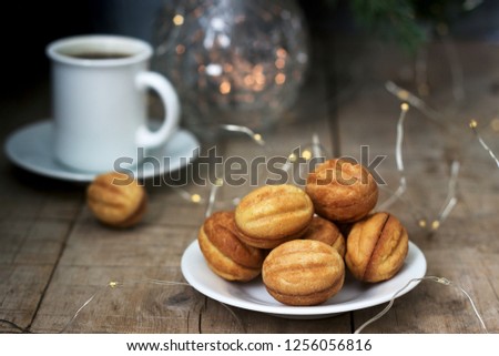 Homemade shortbread cookies in the shape of nuts on the background of a cup of coffee, fir branches and garlands.
