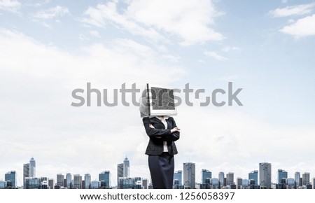 Cropped image of business woman in suit with monitor instead of head keeping arms crossed while standing outdoors with cityscape view on background.