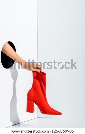 cropped image of girl holding red stylish high heel in hand through hole on white