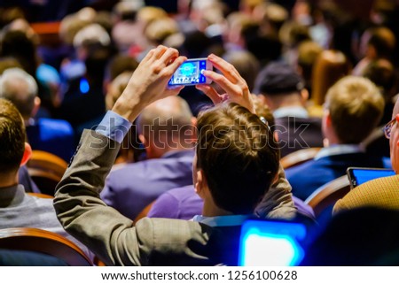 Man takes a picture of the presentation at the conference hall using smartphone