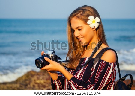 tropical enjoyment summertime tourism and photography. Young traveling woman in a stylish striped jumpsuit with camera and backpack near sea beach indian ocean goa turquoise water, sky and rocks