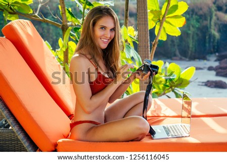 Female european photographer photographing with digital camera on the beach.beautiful woman in coral bikini swimsuit in the tropical paradise sea taking pictures of the landscape photo shoot