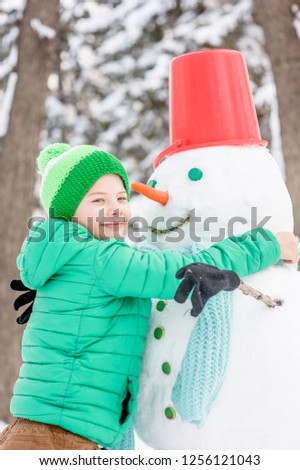 Smiling little boy embraing snowman 