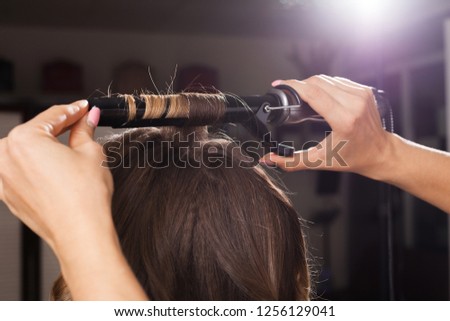 professional hairdresser making a hair curling to a client with long hair in a beauty salon. concept of stylist training Royalty-Free Stock Photo #1256129041
