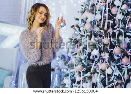 Young beautiful girl in a sweater decorates the Christmas tree