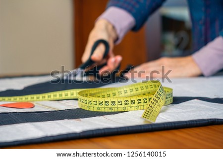 Measuring tape with dressmaker cutting fabric with scissors in the background. Selective focus on measuring tape on foreground