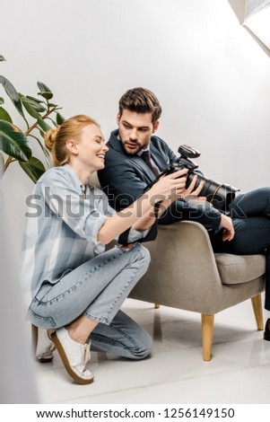 smiling female photographer and handsome businessman using camera in photo studio 