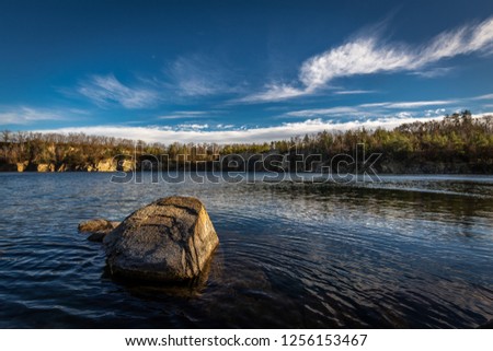 Scenic photo of flooded quarry near Masovice, Znojmo, Czech Republic with roc in the foreground and dark blue sky with white clouds