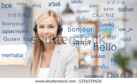translation, business and technology concept - smiling female translator or operator in headset at office over greeting words in different foreign languages