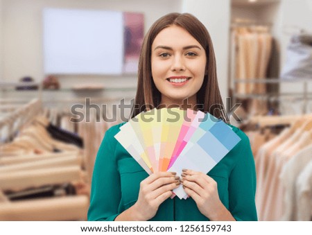 fashion, style and shopping concept - smiling young woman with color swatches or samples over clothing store background