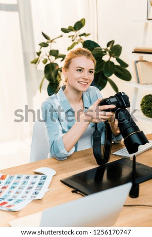 beautiful smiling young photographer holding camera while working in office 