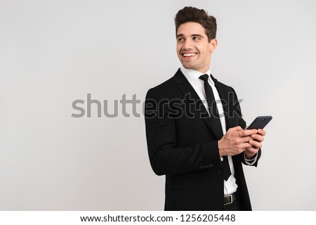 Handsome business man wearing suit standing isolated over gray background, using mobile phone
