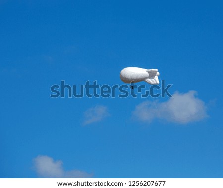 Large white air balloon in the shape of an airship with camera on the background of blue sky