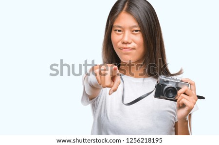 Young asian woman holding vintagera photo camera over isolated background pointing with finger to the camera and to you, hand sign, positive and confident gesture from the front