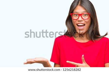 Young asian woman wearing glasses over isolated background amazed and smiling to the camera while presenting with hand and pointing with finger.