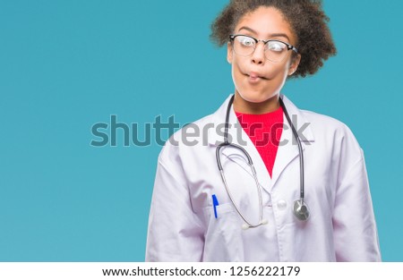 Young afro american doctor woman over isolated background making fish face with lips, crazy and comical gesture. Funny expression.