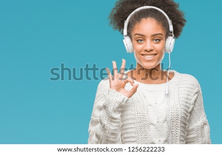 Young afro american woman wearing headphones over isolated background doing ok sign with fingers, excellent symbol