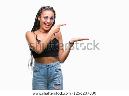 Young braided hair african american with birth mark wearing sunglasses over isolated background amazed and smiling to the camera while presenting with hand and pointing with finger.