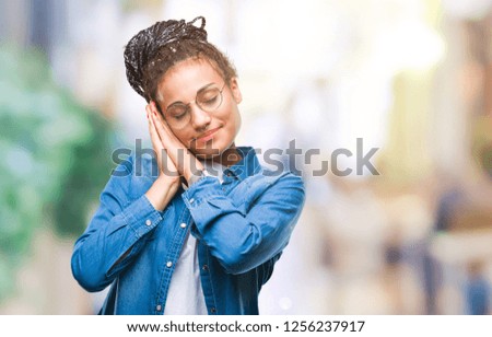 Young braided hair african american girl wearing glasses over isolated background sleeping tired dreaming and posing with hands together while smiling with closed eyes.