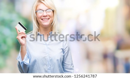 Young beautiful blonde business woman holding credit card over isolated background with a happy face standing and smiling with a confident smile showing teeth