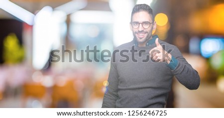Young handsome man wearing glasses over isolated background doing happy thumbs up gesture with hand. Approving expression looking at the camera showing success.