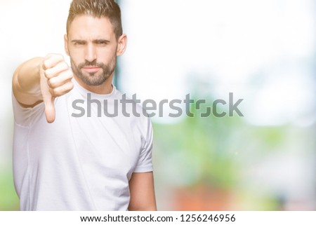 Young man wearing casual white t-shirt over isolated background looking unhappy and angry showing rejection and negative with thumbs down gesture. Bad expression.