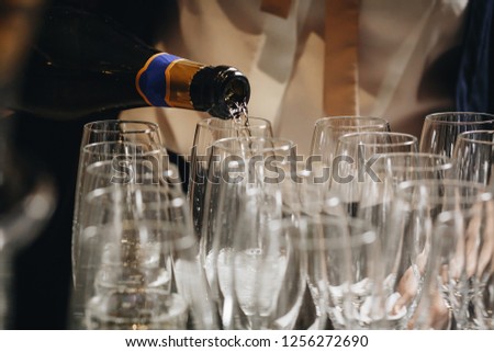 Hand of the waiter pours white wine or champagne in wineglass. Bright picture of pouring wine into glasses