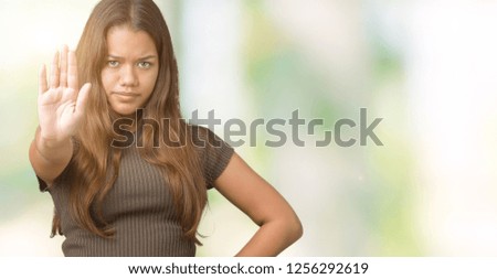 Young beautiful brunette woman over isolated background doing stop sing with palm of the hand. Warning expression with negative and serious gesture on the face.