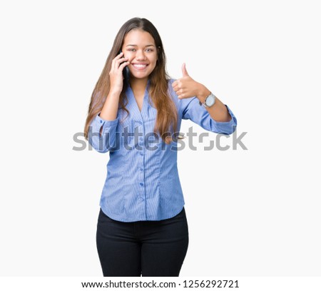 Young beautiful brunette business woman talking on smartphone over isolated background happy with big smile doing ok sign, thumb up with fingers, excellent sign