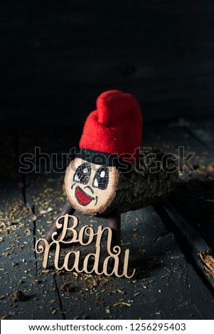 a handmade tio de nadal, a typical christmas character of catalonia, spain, and the text bon nadal, merry christmas written in catalan, on a gray rustic wooden surface, slightly lighted Royalty-Free Stock Photo #1256295403