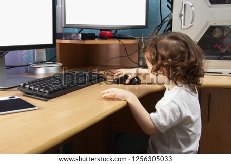 Little 2 3 year old baby girl in white clothers draws at the home computer in graphics drawing tablet. two monitors. The child is holding a mouse. Mock up vith copy space for text.