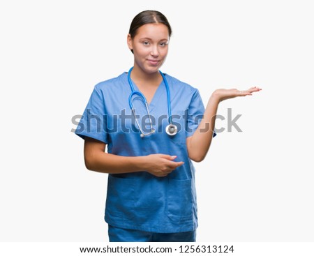 Young caucasian doctor woman wearing medical uniform over isolated background smiling cheerful presenting and pointing with palm of hand looking at the camera.