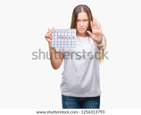 Young caucasian woman holding menstruation calendar over isolated background with open hand doing stop sign with serious and confident expression, defense gesture