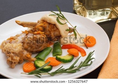 Rabbit legs baked in white wine with bechamel sauce on a ceramic plate with vegetables and rosemary. Dietary rabbit meat cooked in oven.