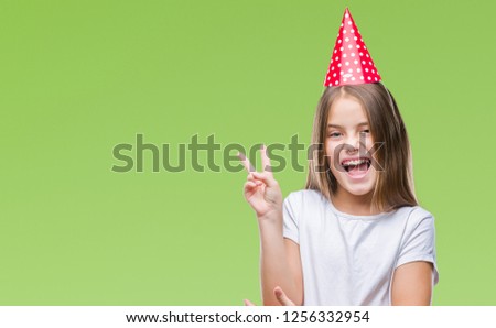 Young beautiful girl wearing birthday cap over isolated background smiling with happy face winking at the camera doing victory sign. Number two.