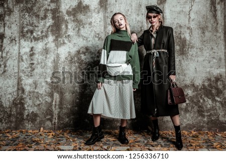 Photo models. Two trendy appealing slim photo models posing near grey wall wearing stylish clothes Royalty-Free Stock Photo #1256336710