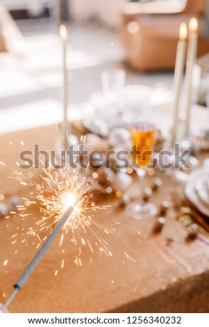 New Year 2021. New Year mood. Table with a gold tablecloth, decorated with candles and tableware for celebration. Festive still life by candlelight. Bengal lights in the foreground. Close-up.