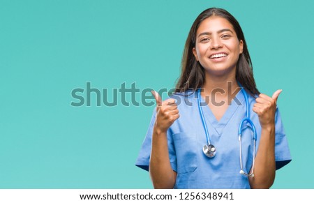 Young arab doctor surgeon woman over isolated background success sign doing positive gesture with hand, thumbs up smiling and happy. Looking at the camera with cheerful expression, winner gesture.