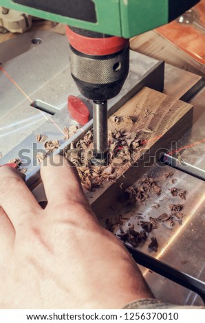 Drill mill for tree in the boring machine with a laser marking. Hands master drills a hole in a wooden bar.