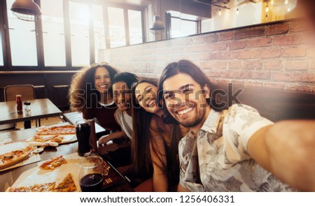 Young man taking selfie with friends sitting at cafe. Group of multi-ethnic friends at restaurant capturing a moment in camera.